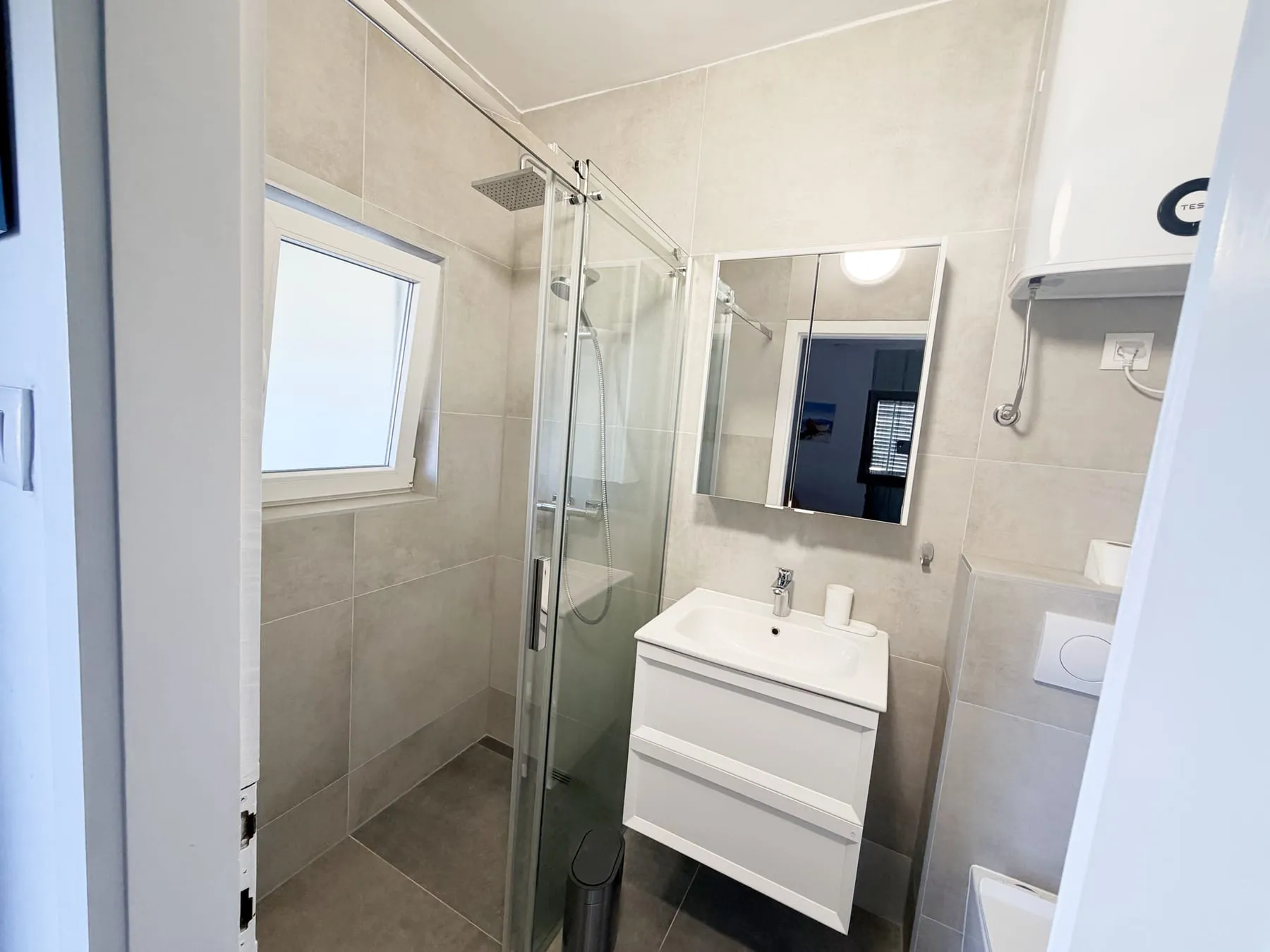 Corner shower with sliding glass doors next to the basin, with a window above