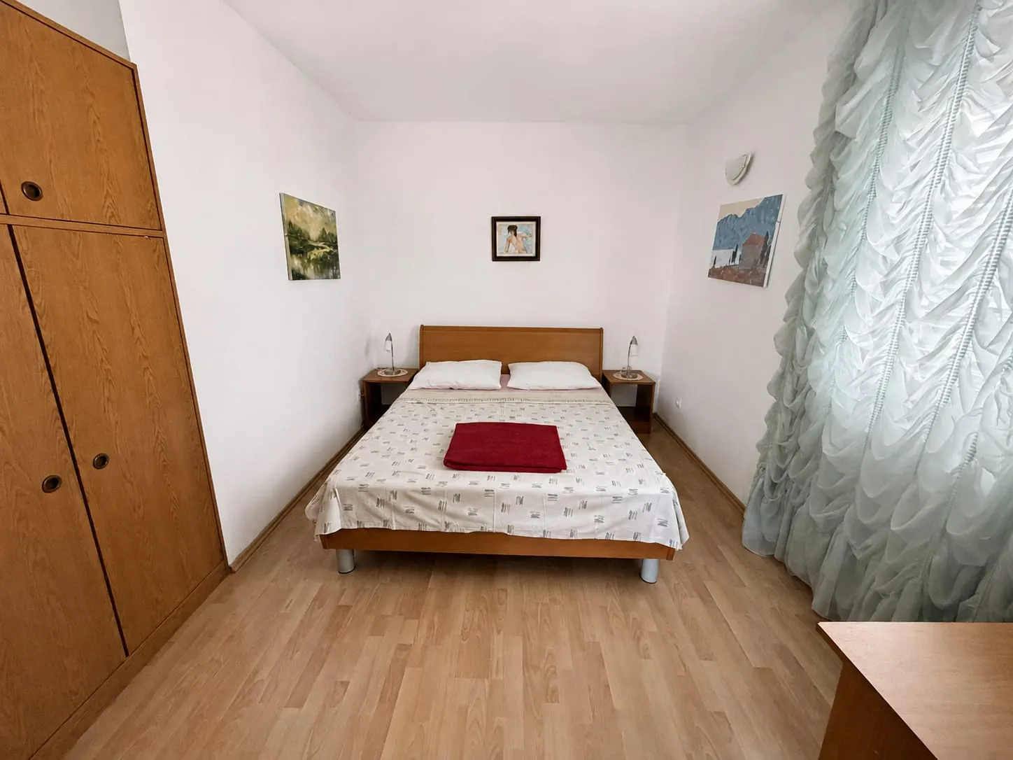 Double bed with a wooden headboard between two lamps, and a wardrobe beside it