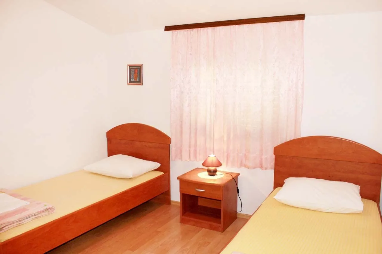 Two single beds either side of a bedside table with a lit lamp, and a curtained window