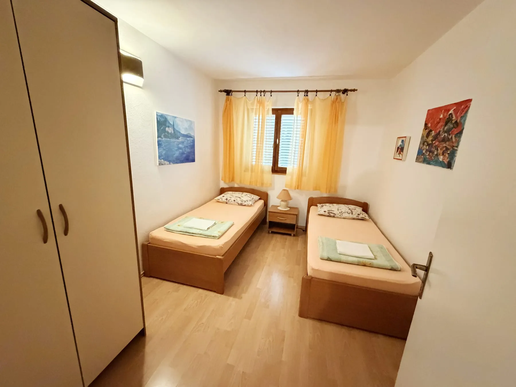 Bedroom with two single beds either side of a bedside table, below a shuttered window