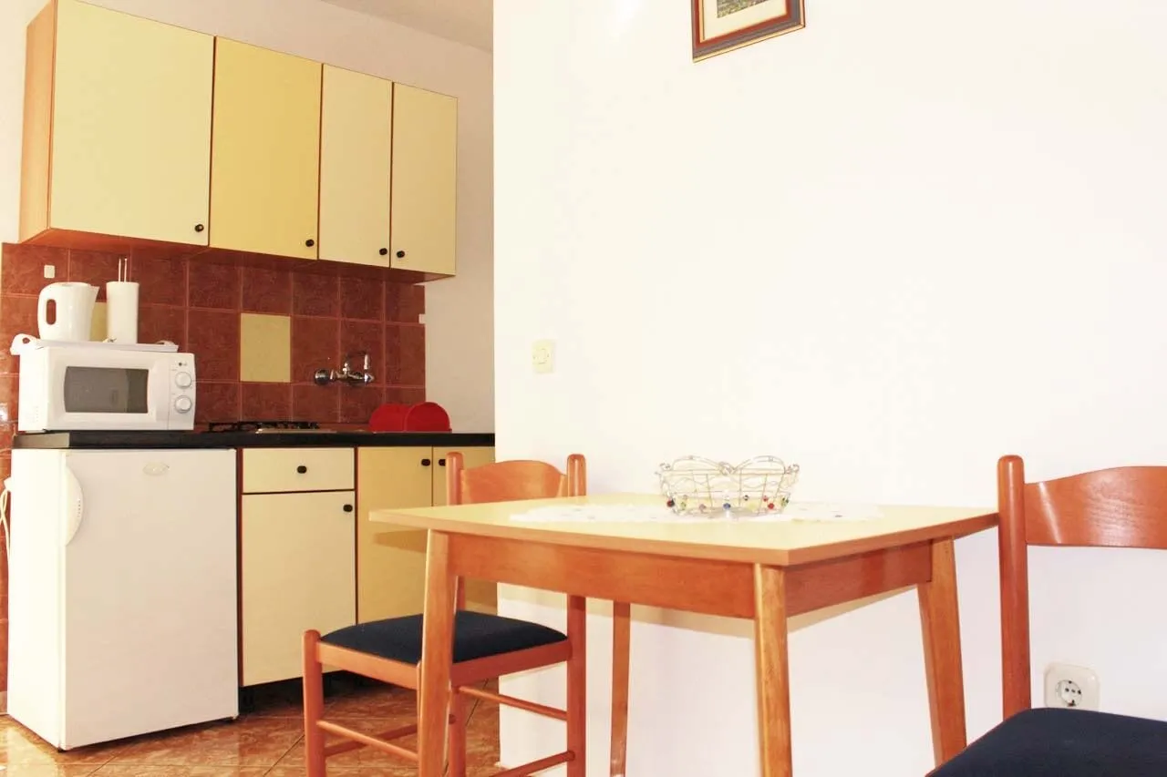 Kitchen with yellow cupboards, a gas hob, a microwave on the fridge, and a dining table