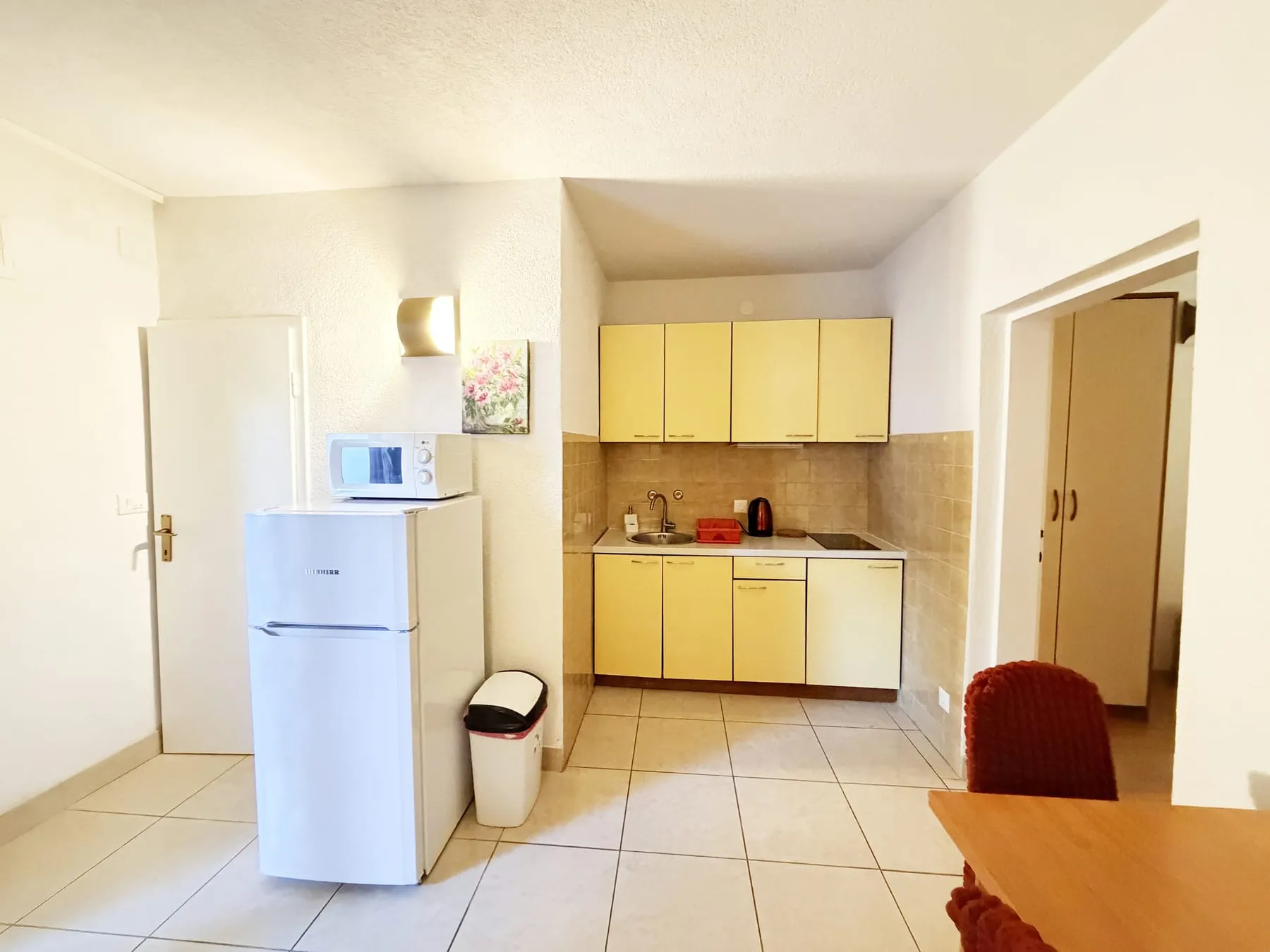 Kitchen with yellow cupboards, a sink, a hob, and a fridge with a microwave on top