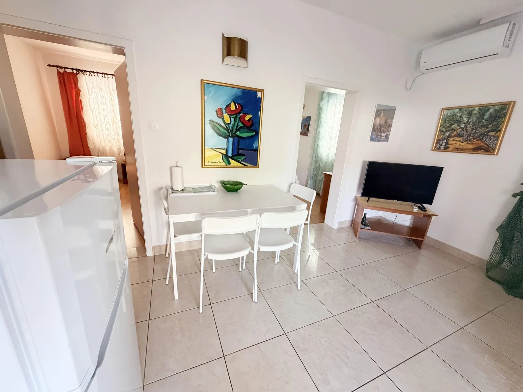 White dining table and chairs, with the fridge on one side and the TV on the other