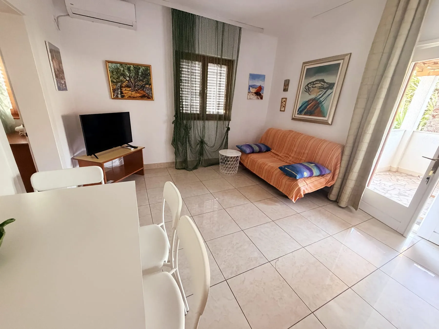 Living room with an orange sofa, a TV on a wooden stand, and an open door to the terrace