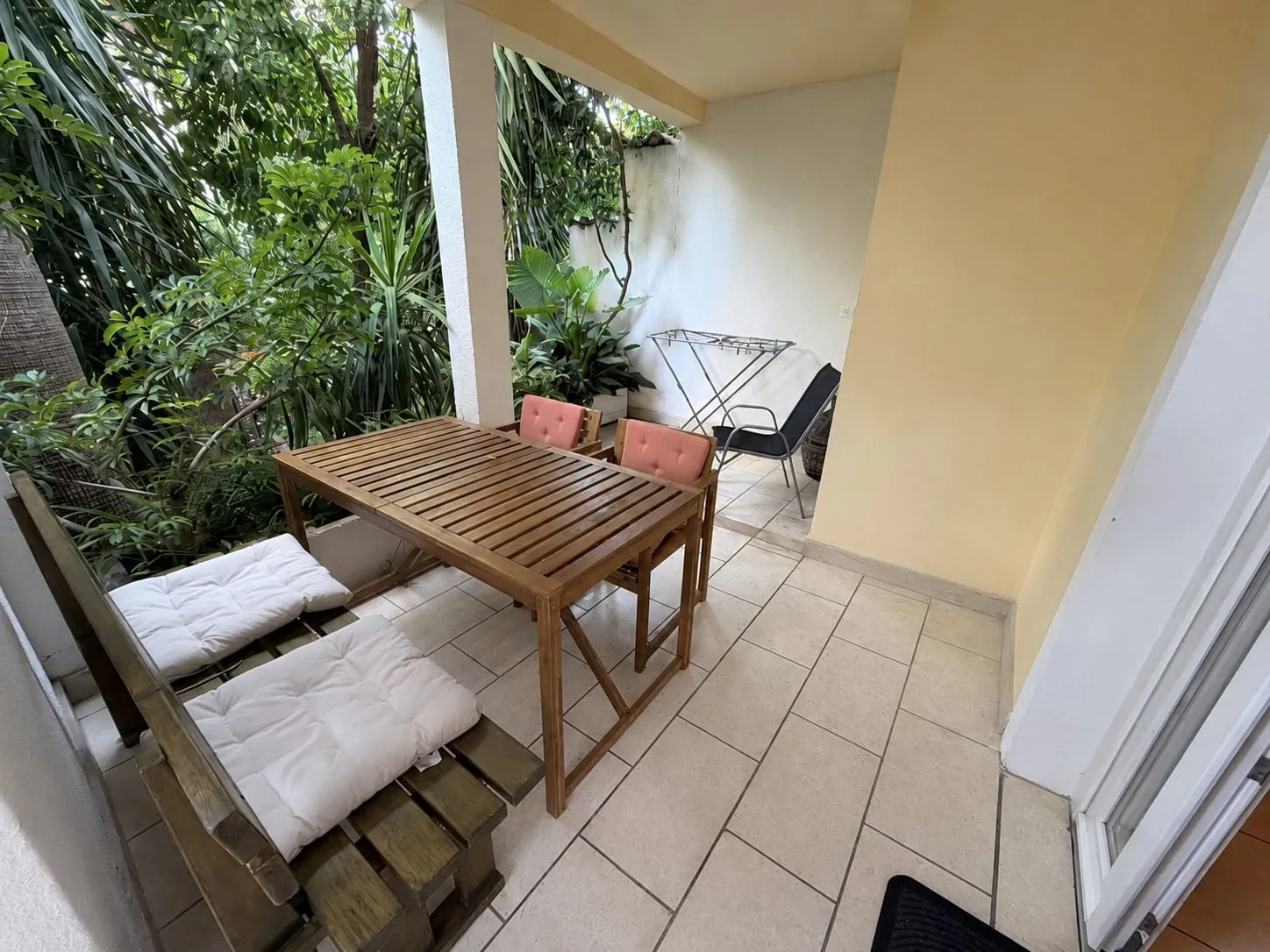 Wooden table and a cushioned bench on the tiled terrace, with greenery beyond